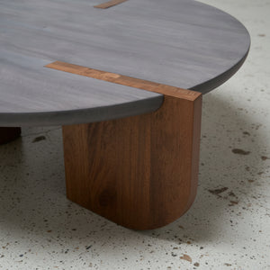 Close-up of a modern table with a wooden leg and gray top on a concrete floor.
