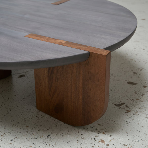 Close-up of a modern table with a wooden leg and gray top on a concrete floor.