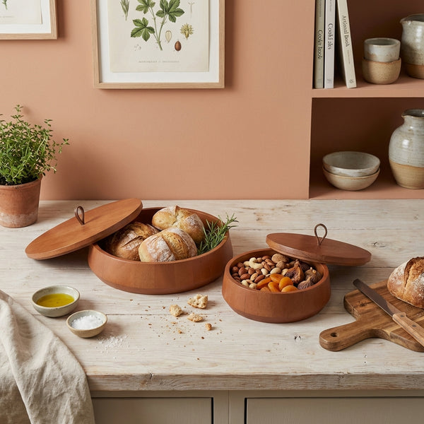 Terracotta bowls with food on a wooden table, with a plant and books in the background.