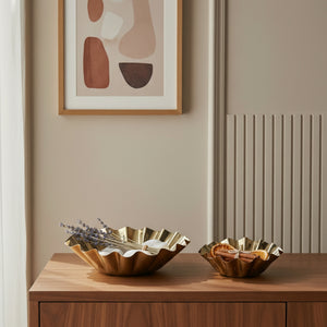 Two gold leaf bowls on a wooden surface with abstract art in the background.