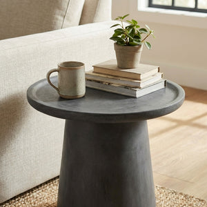 Small round side table with a mug, books, and a plant in a living room setting.