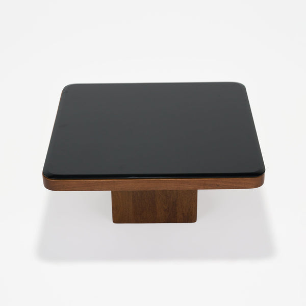 Square table with black top and wooden base on a white background