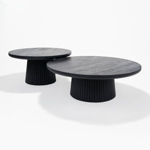 Two round coffee tables with black ribbed bases on a white background