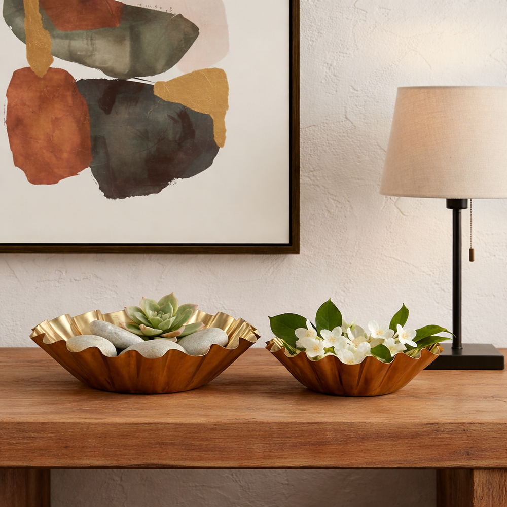 Two gold decorative bowls on a wooden surface with a plant and small elephant figurine in the background.