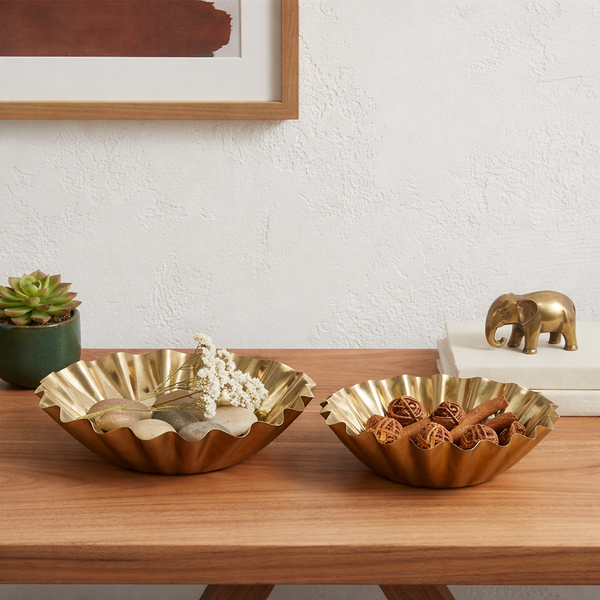 Two gold decorative bowls on a wooden surface with a plant and small elephant figurine in the background.
