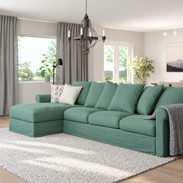 A green sectional sofa with a chaise lounge in a bright, modern living room. The sofa features plush cushions, a matching throw blanket draped over one arm, and is styled on a textured white rug with a light wood floor.