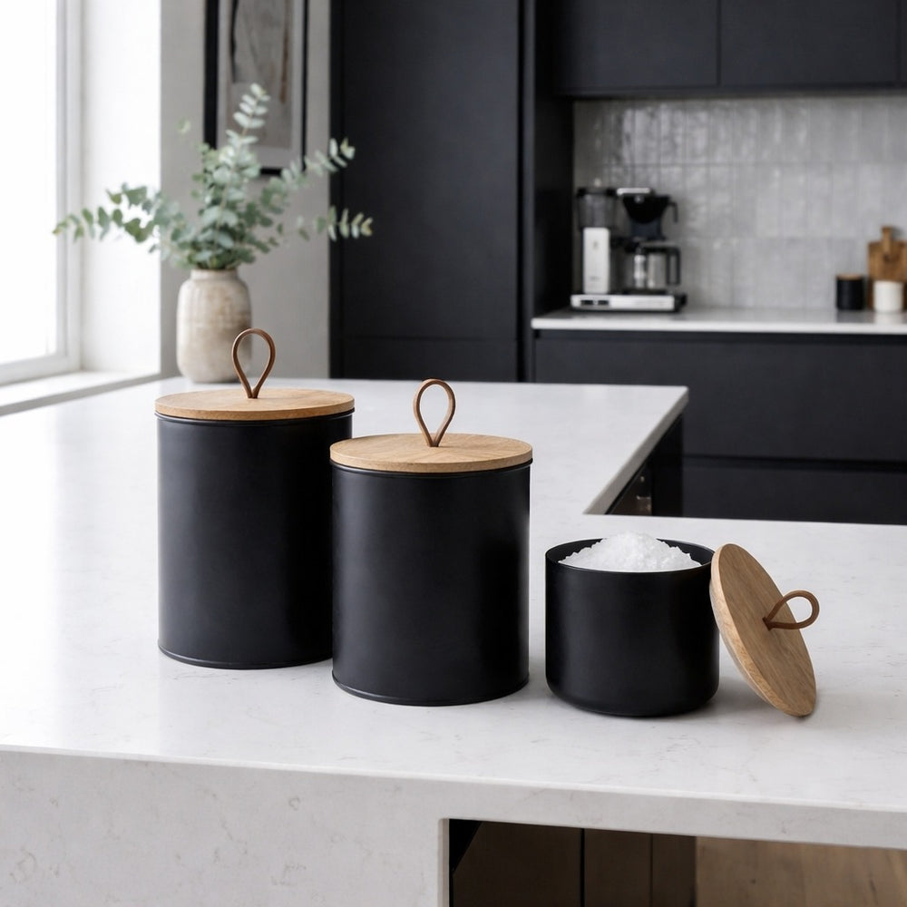 Three black canisters with wooden lids on a kitchen counter.