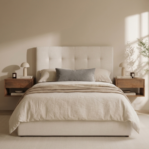A neatly made bed with cream bedding and a gray accent pillow, set in a minimalist bedroom with a tufted cream headboard, wooden nightstands, and soft sunlight streaming in from the side.