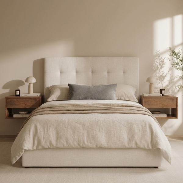 A neatly made bed with cream bedding and a gray accent pillow, set in a minimalist bedroom with a tufted cream headboard, wooden nightstands, and soft sunlight streaming in from the side.