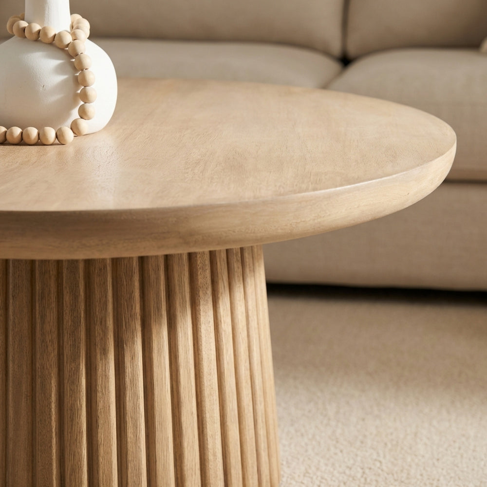 Round wooden coffee table with decorative items in a living room setting.