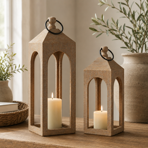 Two wooden lanterns with candles inside on a table with plants and books in the background.