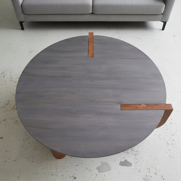 Round wooden coffee table with bronze legs in a minimalistic living room setting.