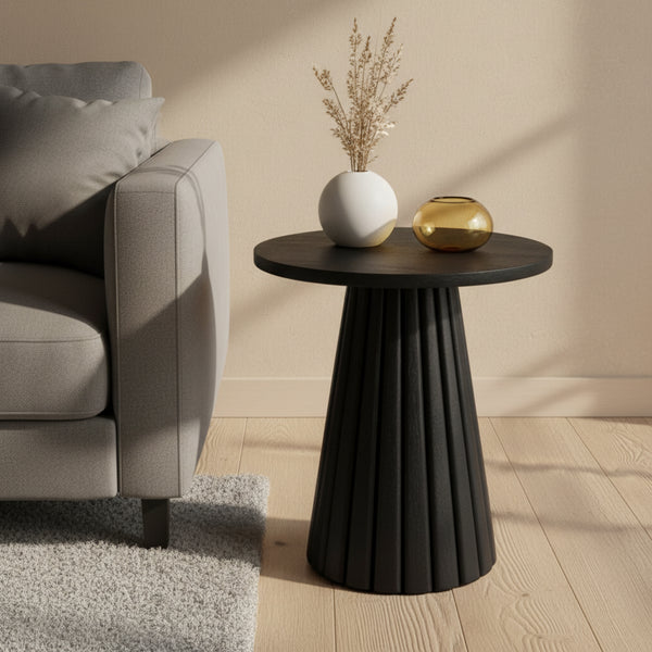 Black side table with decorative items next to a gray sofa in a living room setting.